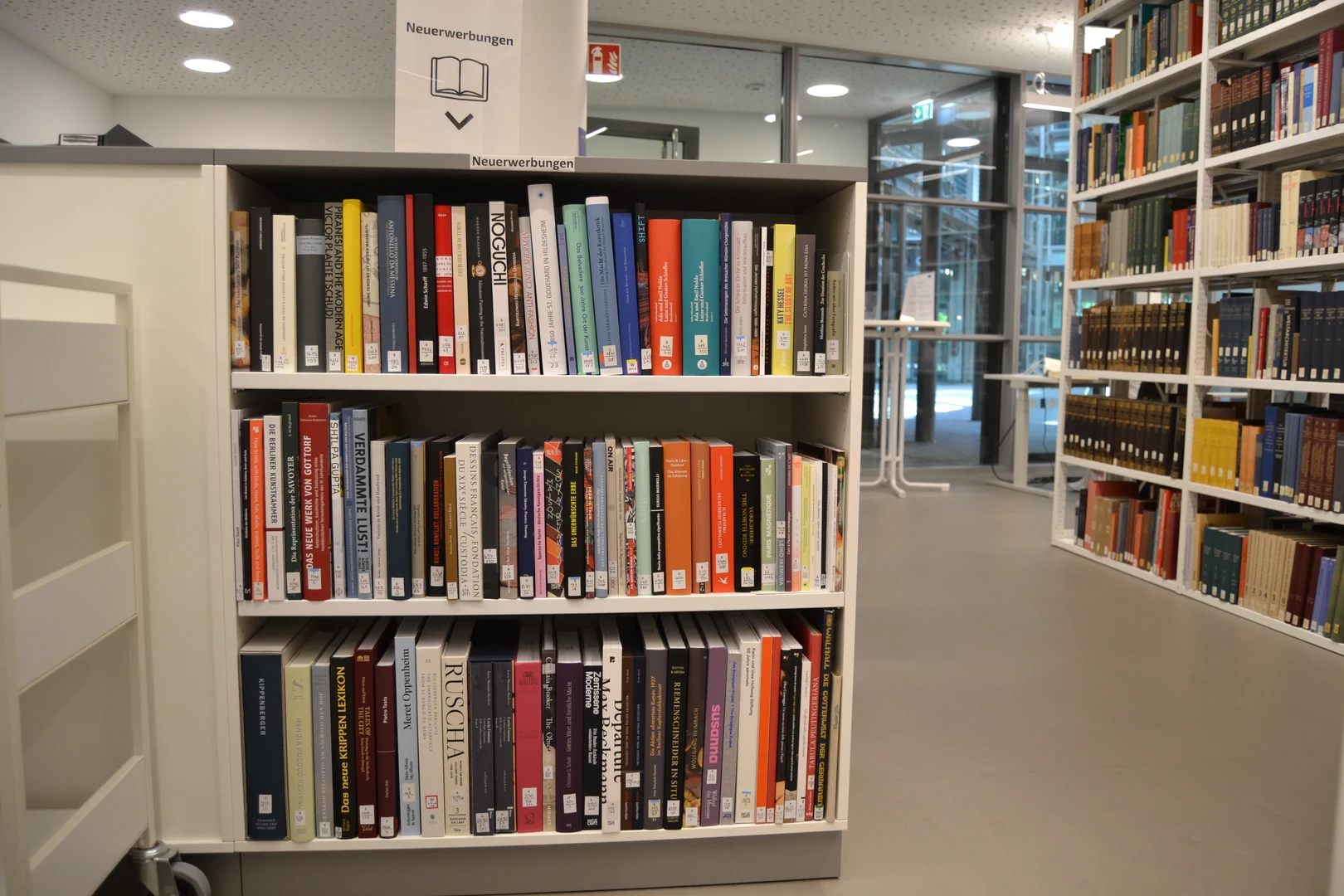 Eine Wissenschaftlerin und ein Wissenschaftler arbeiten hinter einer Glasfassade und mischen Chemikalien mit Großgeräten.