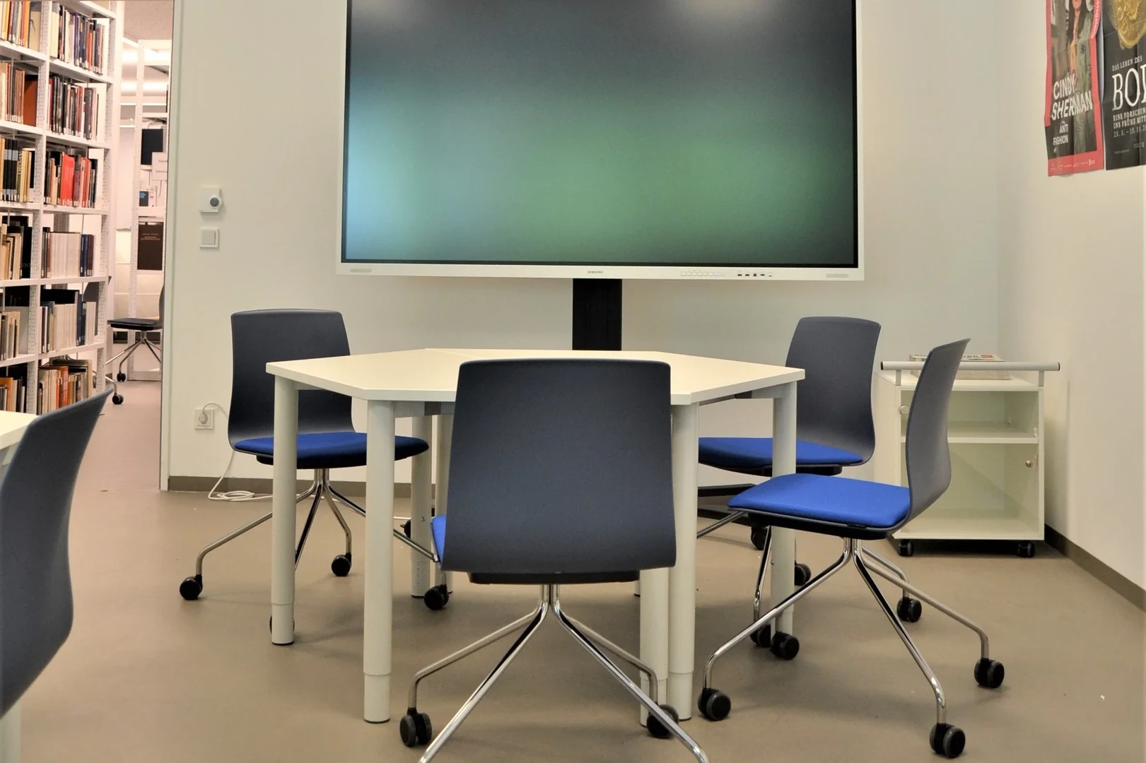 Eine Wissenschaftlerin und ein Wissenschaftler arbeiten hinter einer Glasfassade und mischen Chemikalien mit Großgeräten.