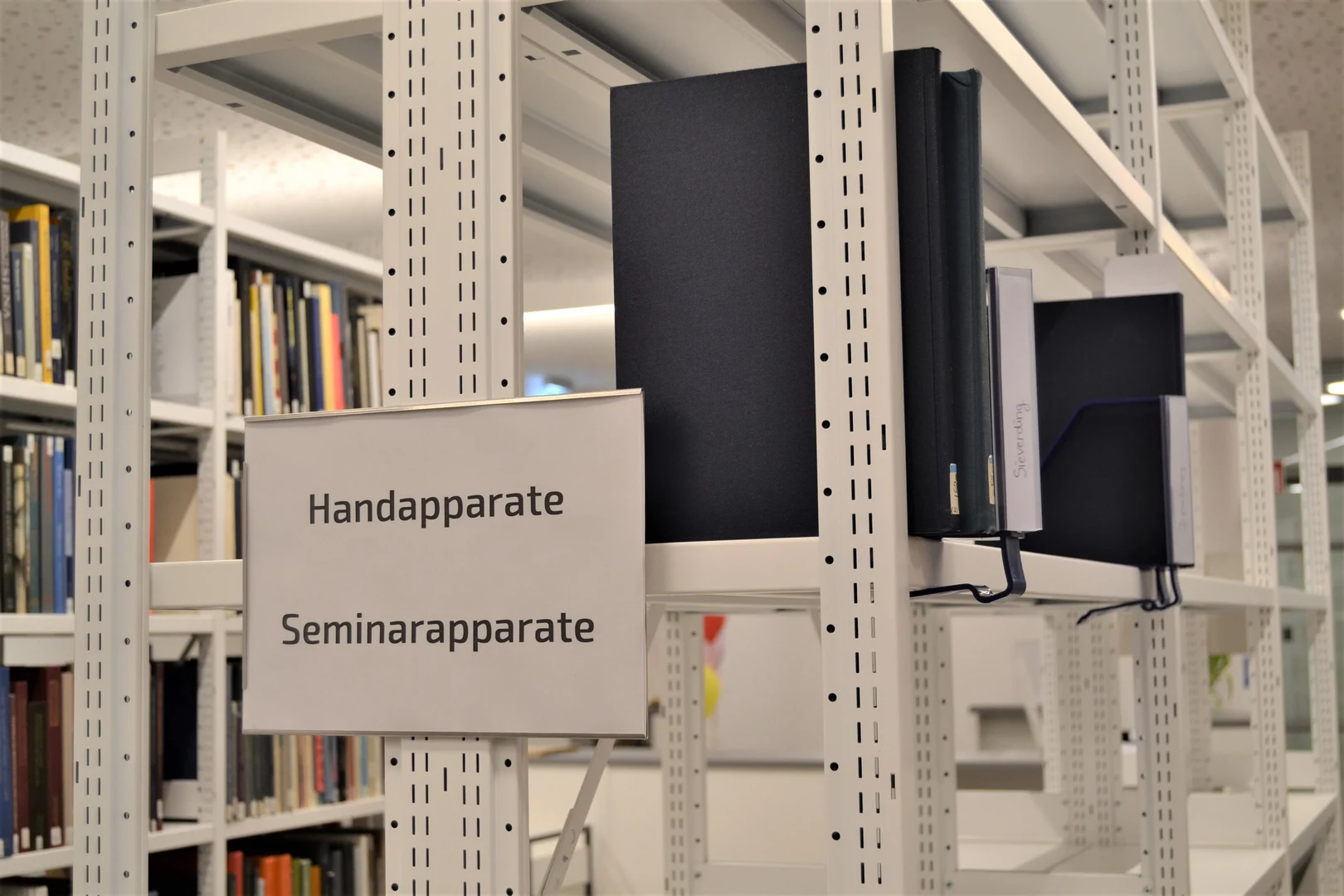 Eine Wissenschaftlerin und ein Wissenschaftler arbeiten hinter einer Glasfassade und mischen Chemikalien mit Großgeräten.