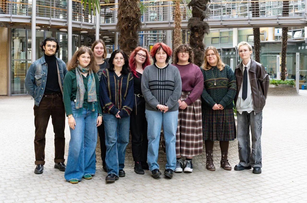 Eine Wissenschaftlerin und ein Wissenschaftler arbeiten hinter einer Glasfassade und mischen Chemikalien mit Großgeräten.