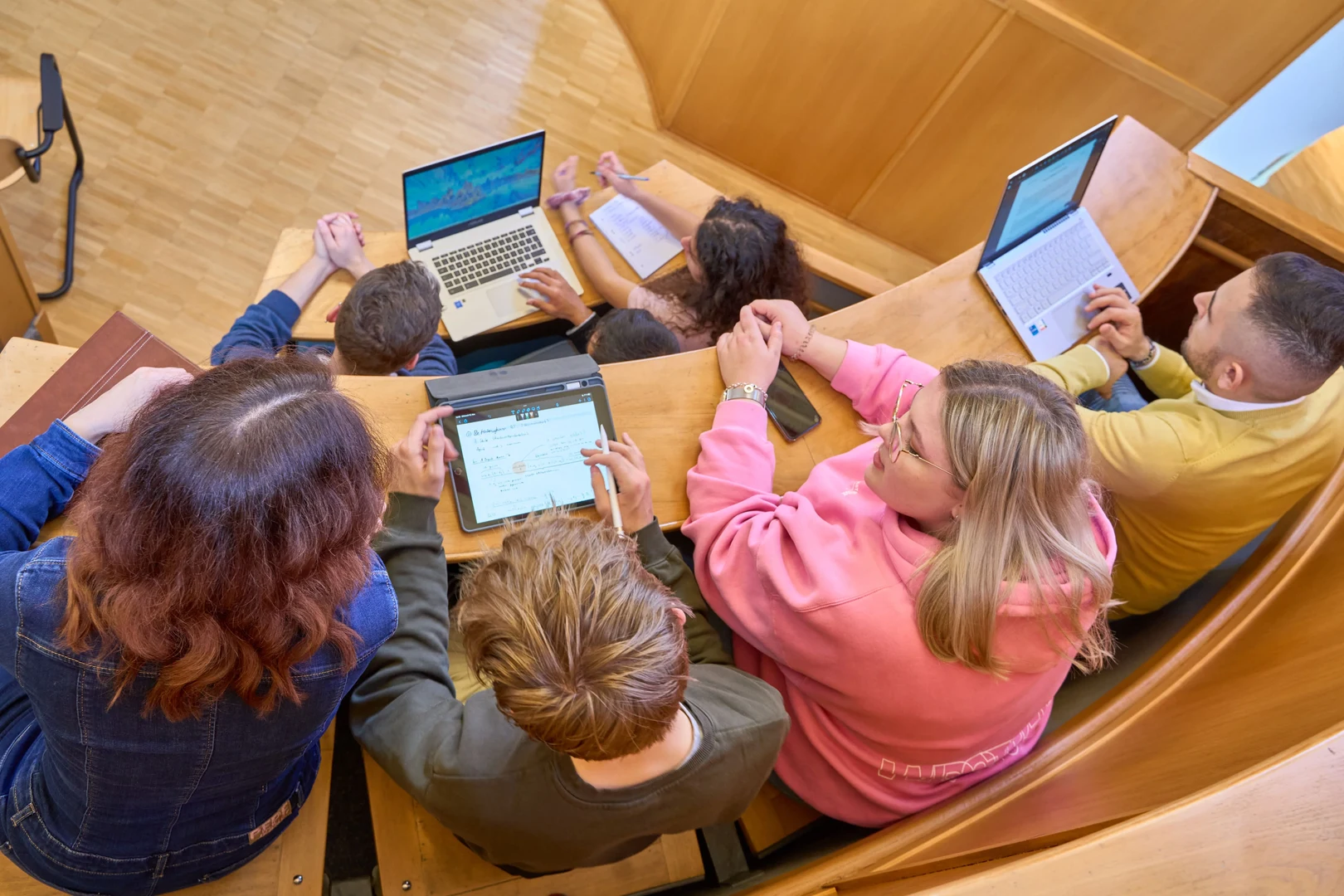 Eine Wissenschaftlerin und ein Wissenschaftler arbeiten hinter einer Glasfassade und mischen Chemikalien mit Großgeräten.