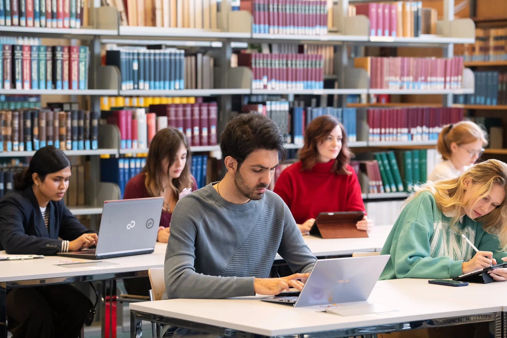 Eine Wissenschaftlerin und ein Wissenschaftler arbeiten hinter einer Glasfassade und mischen Chemikalien mit Großgeräten.